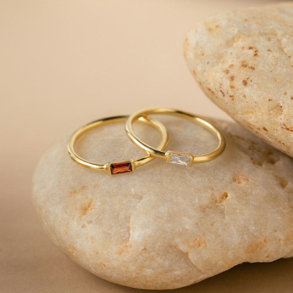 two gold wedding rings sitting on top of a rock