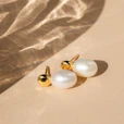 A close-up of delicate gold and pearl earrings resting on soft beige fabric, capturing the essence of understated elegance.