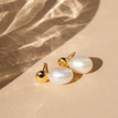 Pair of pearl drop earrings catching light against a soft pastel background.