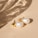 A pair of elegant pearl earrings with gold accents rests on a smooth beige surface. Soft shadows and light reflections create a subtle, sophisticated pattern across the background.
