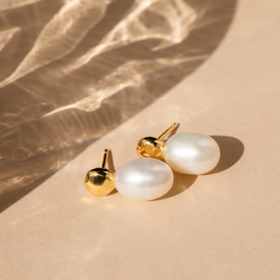 Close-up of elegant white and gold pastel earrings displayed on a soft fabric background