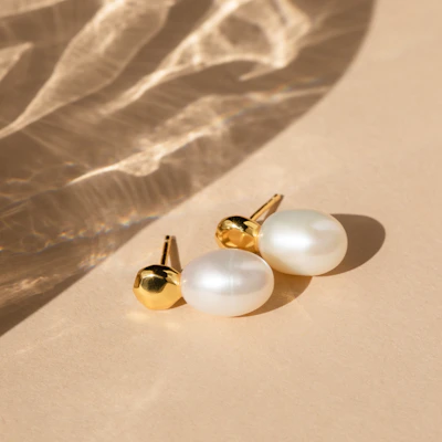 A pair of shimmering gold earrings catching the light against a soft cream background