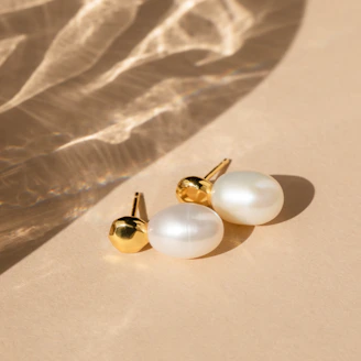 Close-up of delicate gold earrings with subtle diamond accents on a soft beige background
