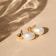 Close-up of a delicate pearl earring from elizabetheh llc resting on a soft fabric background.