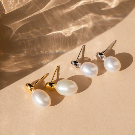 Elegant display of gold and pearl earrings on a minimalist white surface with gentle shadows.