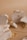 A collection of gold jewelry, including chains, rings, and bracelets, is artfully arranged on pieces of rough white stone. The jewelry features various designs and some pieces are adorned with small stones or beads. The backdrop is a neutral, warm beige color that complements the gold tones.