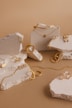 A collection of gold jewelry pieces including necklaces, rings, and earrings is artfully arranged on pieces of textured stone against a light brown background. The jewelry features delicate chain links, engravings, and intricate detailing.