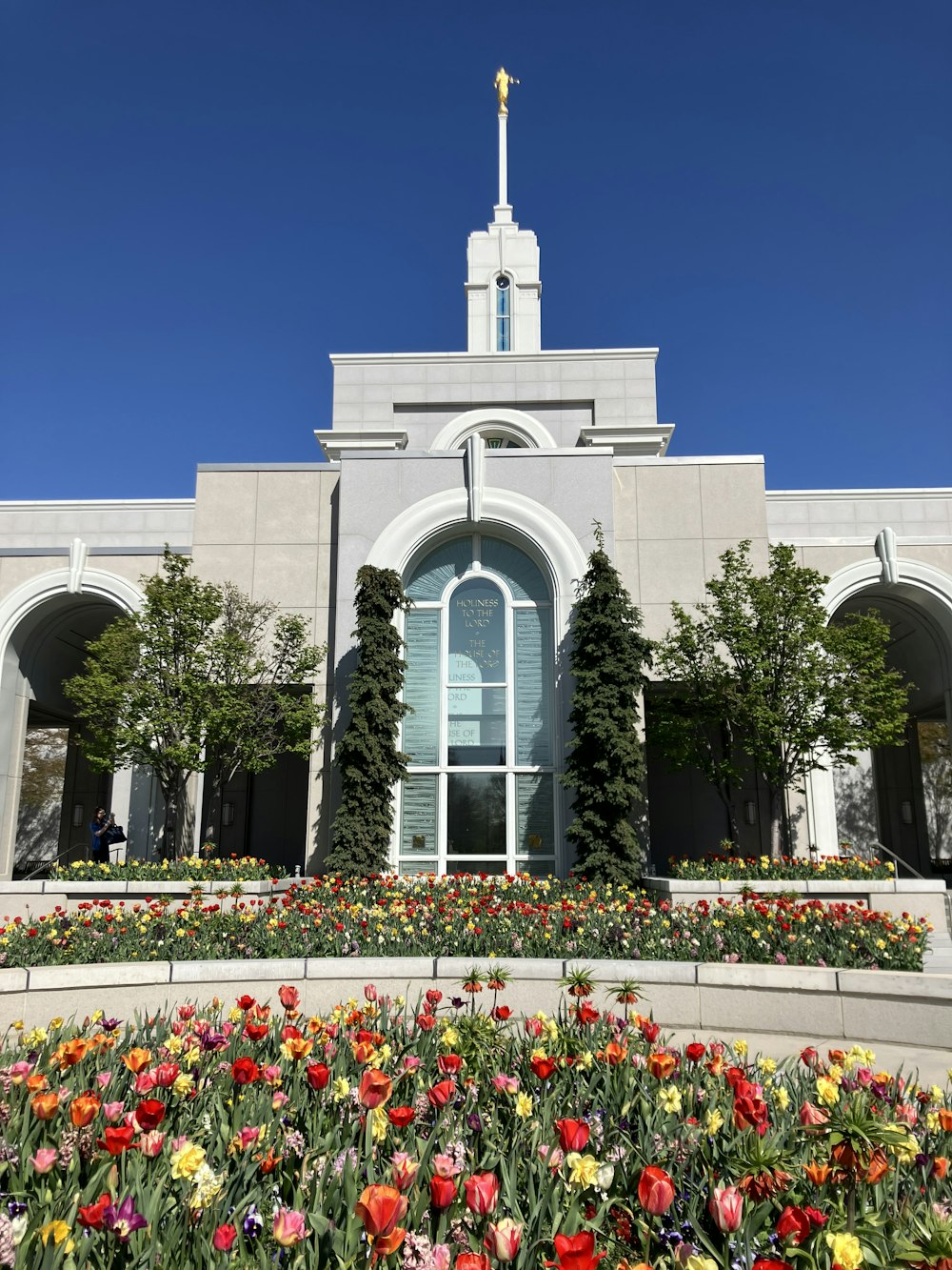 a church with a clock tower and a flower garden in front of it