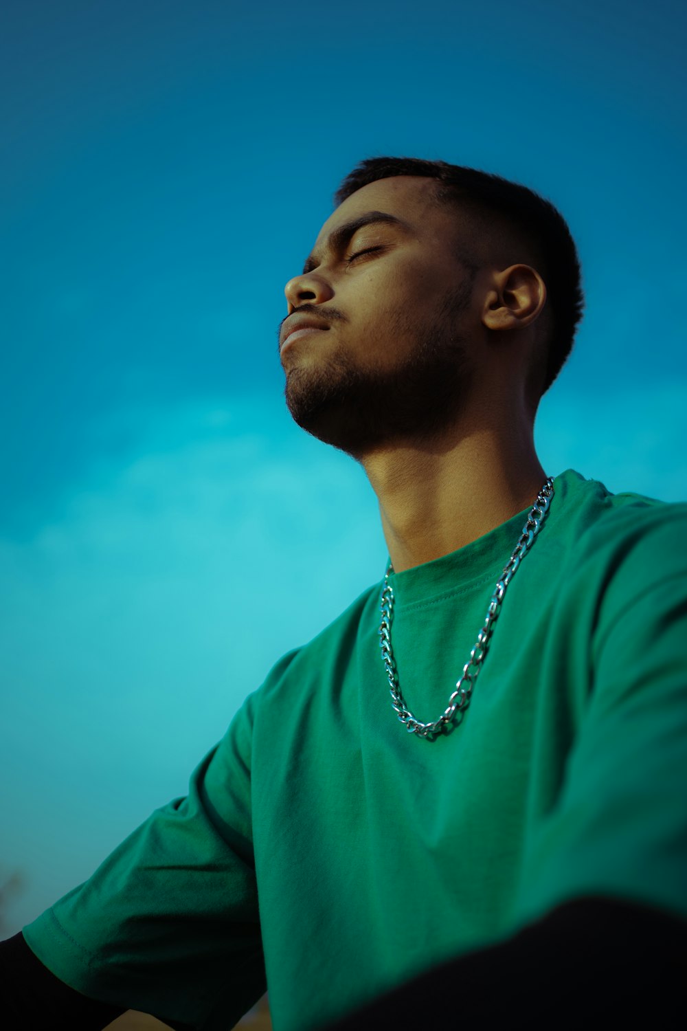 a man wearing a green shirt and a necklace