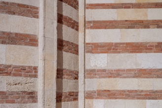 The image features a section of a building's exterior wall with alternating layers of bricks and stone, creating a striped pattern. The colors are predominantly earthy tones of red and beige, highlighting the contrast between the materials. This detailed shot emphasizes the textural elements and architectural design.