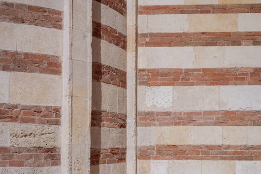 The image features a section of a building's exterior wall with alternating layers of bricks and stone, creating a striped pattern. The colors are predominantly earthy tones of red and beige, highlighting the contrast between the materials. This detailed shot emphasizes the textural elements and architectural design.
