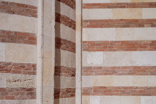 The image features a section of a building's exterior wall with alternating layers of bricks and stone, creating a striped pattern. The colors are predominantly earthy tones of red and beige, highlighting the contrast between the materials. This detailed shot emphasizes the textural elements and architectural design.