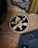A round emblem featuring the words 'Special Forces' and 'Motivated. Dedicated. Lethal.' surrounds a design with arrows, a skull, and a green military helmet with a gold crest. The emblem is on a wooden surface, accompanied by a black tool and a fabric band.