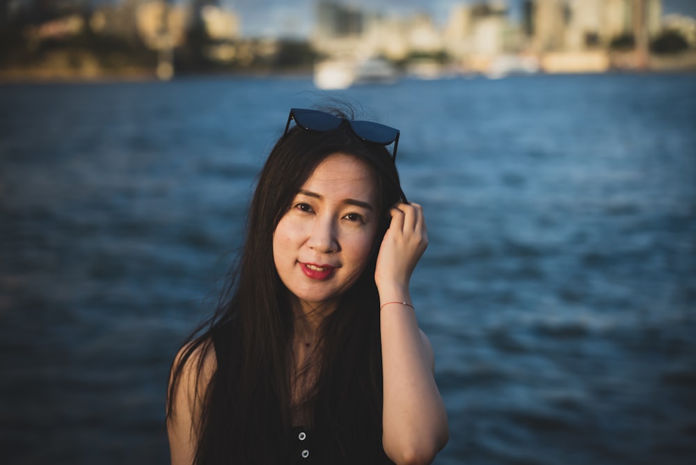 a woman with sunglasses on her head standing next to a body of water