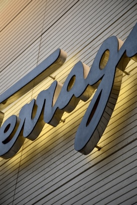 A large, stylized script sign features prominently on a wall with horizontal wooden paneling. The sign is illuminated from behind, casting a warm glow around the letters.