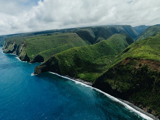 An aerial view of a lush green hillside next to the ocean — Kauaʻi, United States