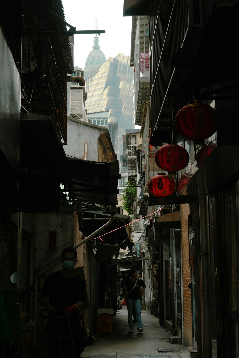 a narrow city street with a few people walking down it