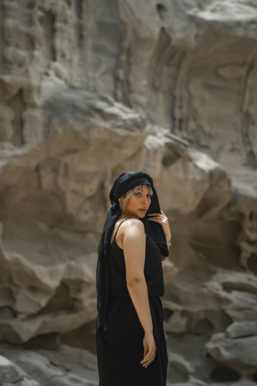 a woman in a black dress standing in front of a rock formation