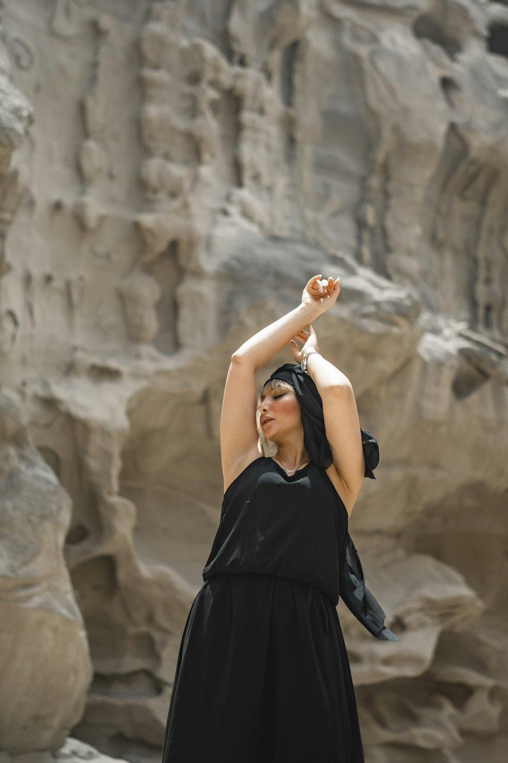 a woman in a black dress standing in front of a rock formation