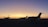 Several private jets are parked on an airport tarmac during a stunning sunset. The sky transitions from a deep blue at the top to a warm orange near the horizon, creating a serene and peaceful atmosphere.