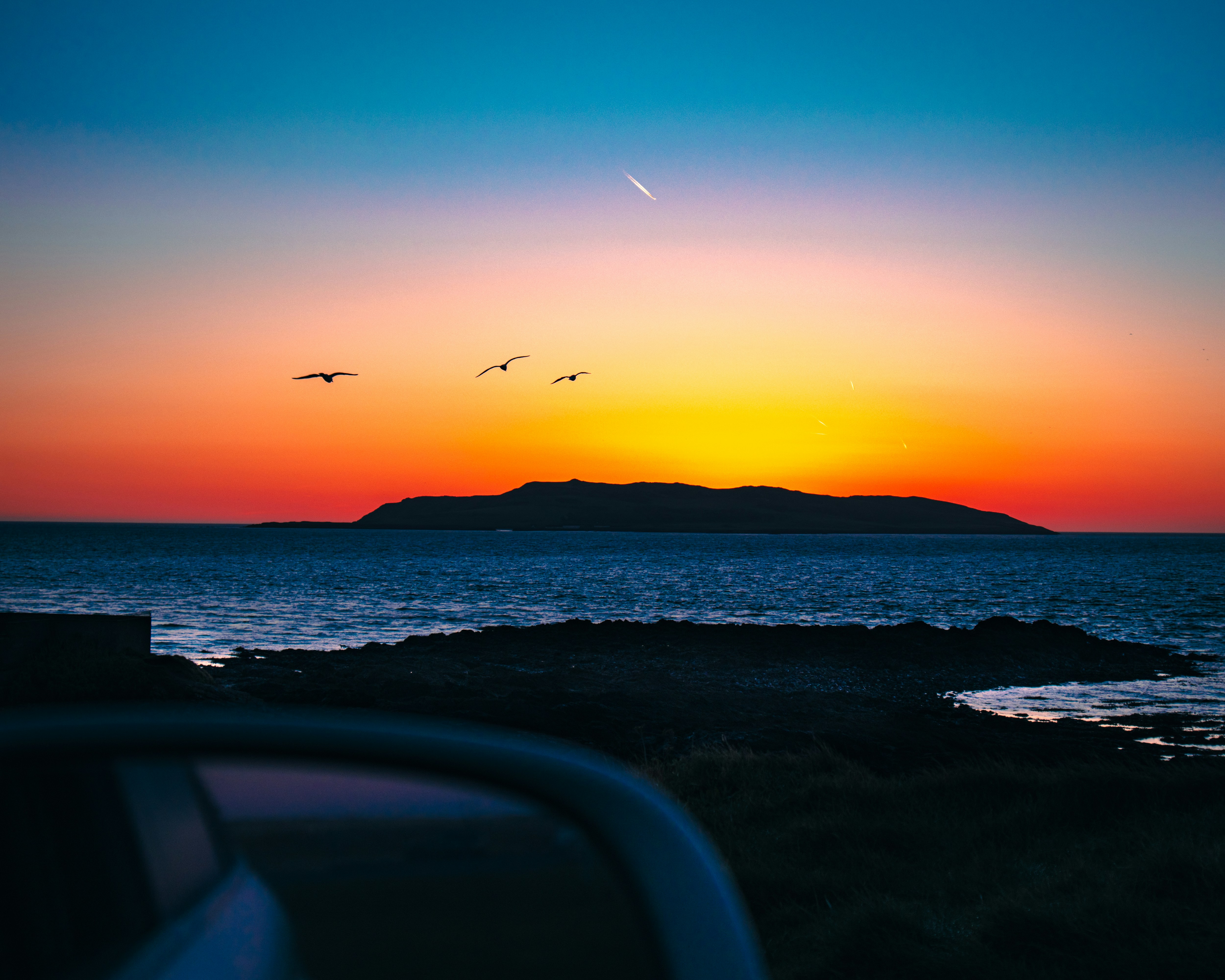 a sunset over a body of water with birds flying in the sky