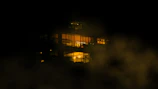 Nighttime view of a soaring glass facade with smoky light reflections and subtle gold accents.