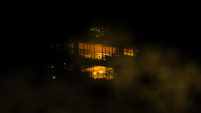 Nighttime view of a soaring glass facade with smoky light reflections and subtle gold accents.
