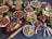 A large assortment of Indian dishes is artfully arranged on a table. The spread includes various curries, shallow-fried breads, grilled meats, fresh salads, and crispy starters. A prominent feature is the vibrant use of spices and colorful garnishes such as fresh herbs and lemon wedges. An array of dips and sauces accompanies the feast.