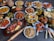 A large assortment of Indian dishes is artfully arranged on a table. The spread includes various curries, shallow-fried breads, grilled meats, fresh salads, and crispy starters. A prominent feature is the vibrant use of spices and colorful garnishes such as fresh herbs and lemon wedges. An array of dips and sauces accompanies the feast.