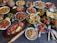 A large assortment of Indian dishes is artfully arranged on a table. The spread includes various curries, shallow-fried breads, grilled meats, fresh salads, and crispy starters. A prominent feature is the vibrant use of spices and colorful garnishes such as fresh herbs and lemon wedges. An array of dips and sauces accompanies the feast.