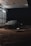 A car is parked in a dimly lit, covered area at night. Overhead lighting casts a soft glow on the vehicle, creating reflections on its surface. The environment appears to be a car wash or service area with metallic siding and a wet ground.