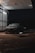 A car is parked in a dimly lit, covered area at night. Overhead lighting casts a soft glow on the vehicle, creating reflections on its surface. The environment appears to be a car wash or service area with metallic siding and a wet ground.