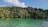 Kayakers paddle on a serene, turquoise river bordered by lush, dense forest under a clear blue sky.