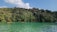 Kayakers paddle on a serene, turquoise river bordered by lush, dense forest under a clear blue sky.