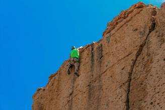 Worker installing a rock anchor on a steep hillside under a clear blue sky.