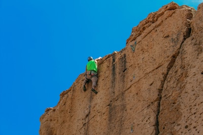 Worker installing a rock anchor on a steep hillside under a clear blue sky.