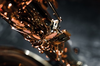 A close-up of a saxophone, highlighting its shiny brass keys and intricate details against a dark, blurred background. The lighting creates warm reflections on the metal surface.