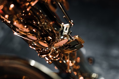 A close-up of a saxophone, highlighting its shiny brass keys and intricate details against a dark, blurred background. The lighting creates warm reflections on the metal surface.