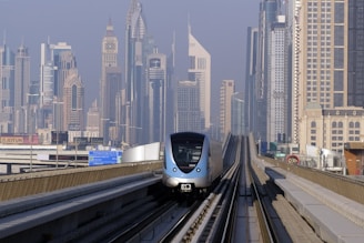 a silver train traveling down train tracks next to tall buildings