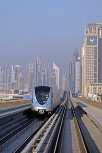 a silver train traveling down train tracks next to tall buildings