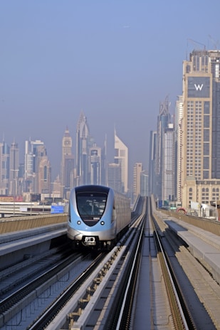 a silver train traveling down train tracks next to tall buildings