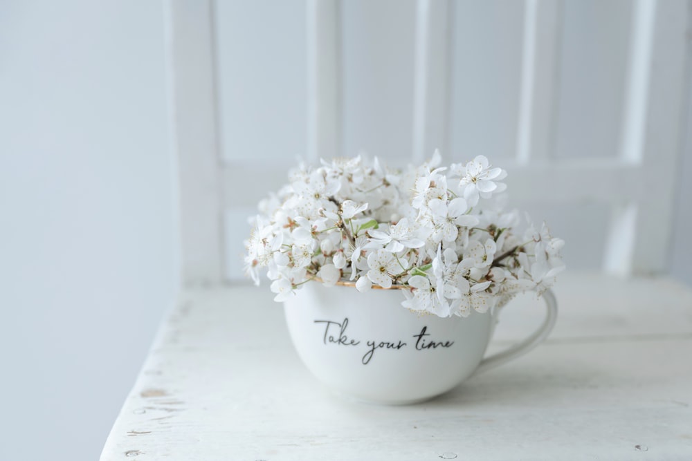 a white cup filled with white flowers on top of a table