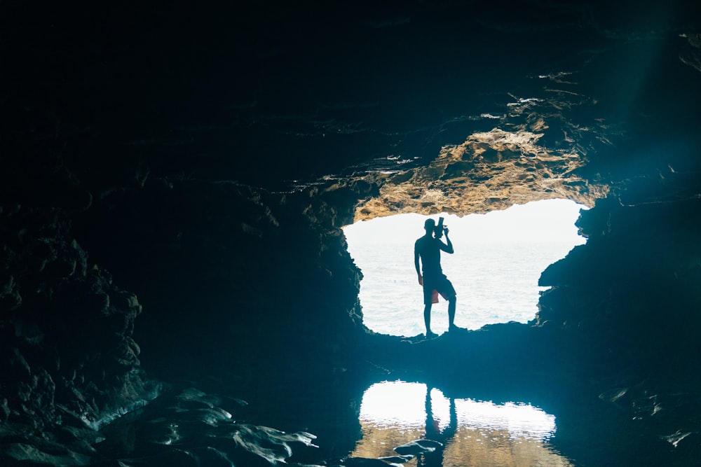 a man standing in a cave looking at the water