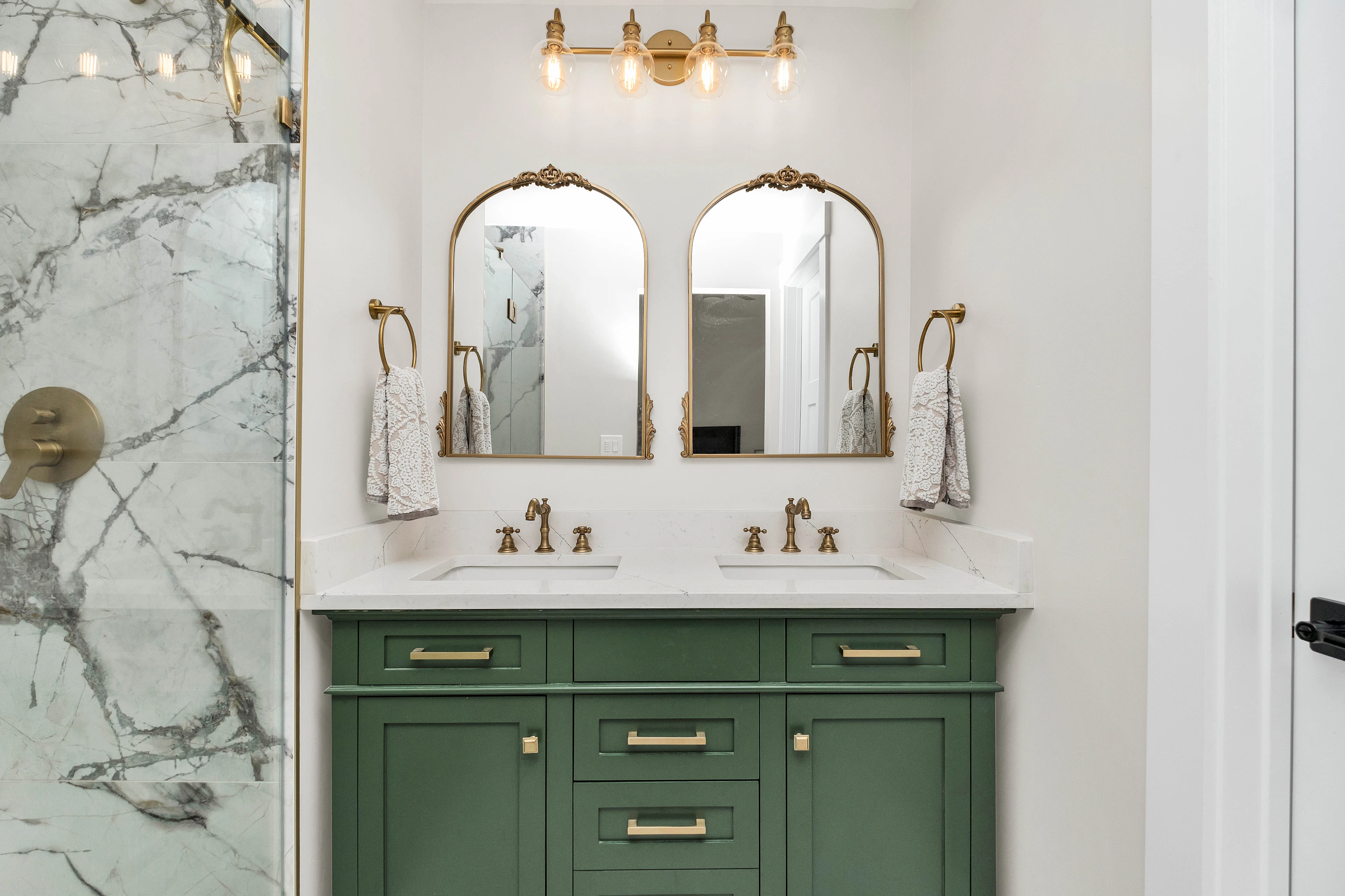 Green double vanity with brass sconces and marble
