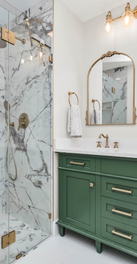 a bathroom with green cabinets and a marble shower