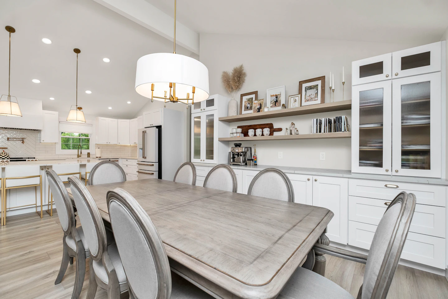 Dining table under a drum chandelier beside glass-front display cabinets