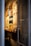 A narrow entryway filled with neatly arranged magazines and brochures on a wooden shelf. The wall features several framed posters, mostly promoting travel and lifestyle content. The ambient lighting casts a warm glow, creating a cozy atmosphere.