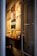 A narrow entryway filled with neatly arranged magazines and brochures on a wooden shelf. The wall features several framed posters, mostly promoting travel and lifestyle content. The ambient lighting casts a warm glow, creating a cozy atmosphere.