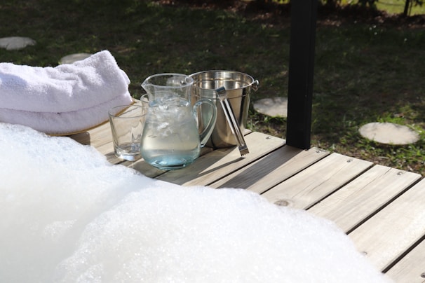 An inviting ice bath filled with clear water, surrounded by towels and a small plant on a wooden deck.