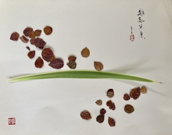 A minimalist composition featuring scattered brown leaves and a single green blade of grass on a textured light surface. Intricate calligraphy and a red stamp add artistic detail to the upper right corner.